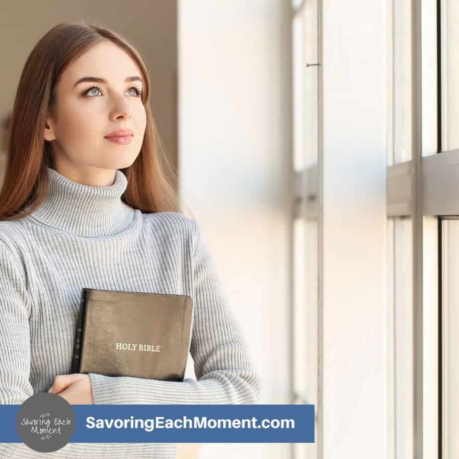 Young woman looking out the window holding a Bible