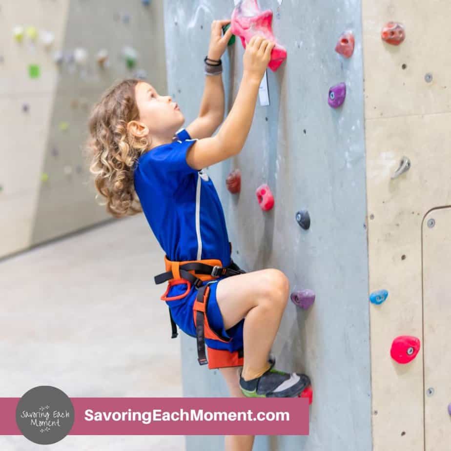 Little girl in blue shirt climbing up a climbing wall at the gym.
